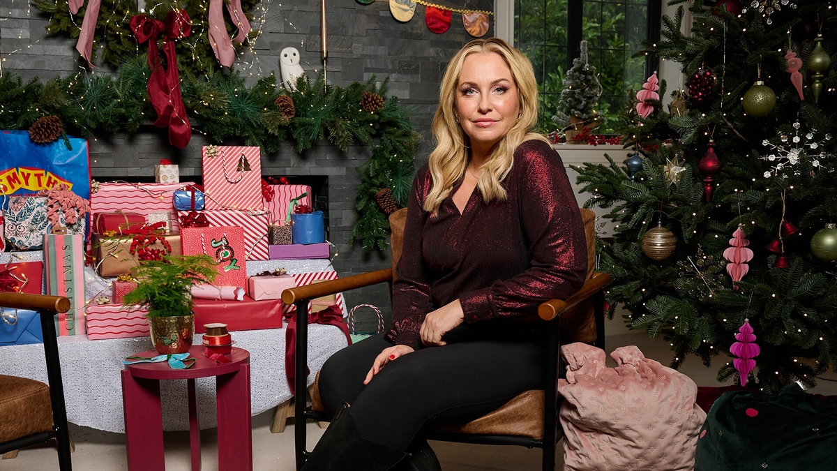 Josie Gibson sits on a chair by a pile of gifts and a Christmas tree