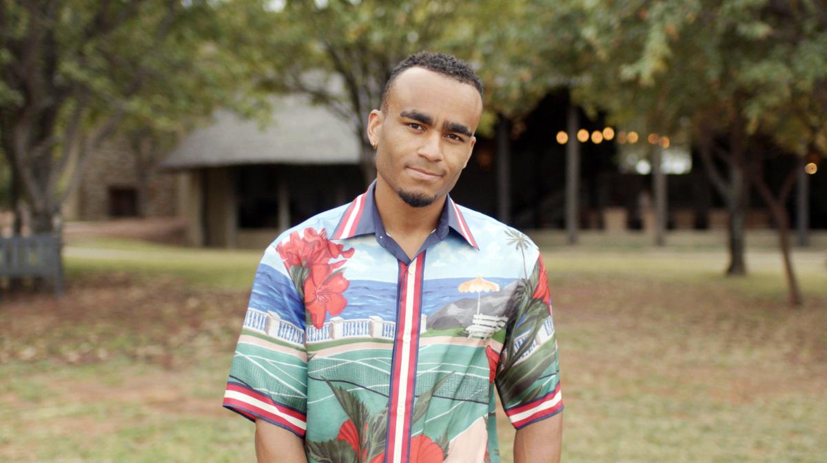 Munya Chawawa stands in a patterned shirt outside