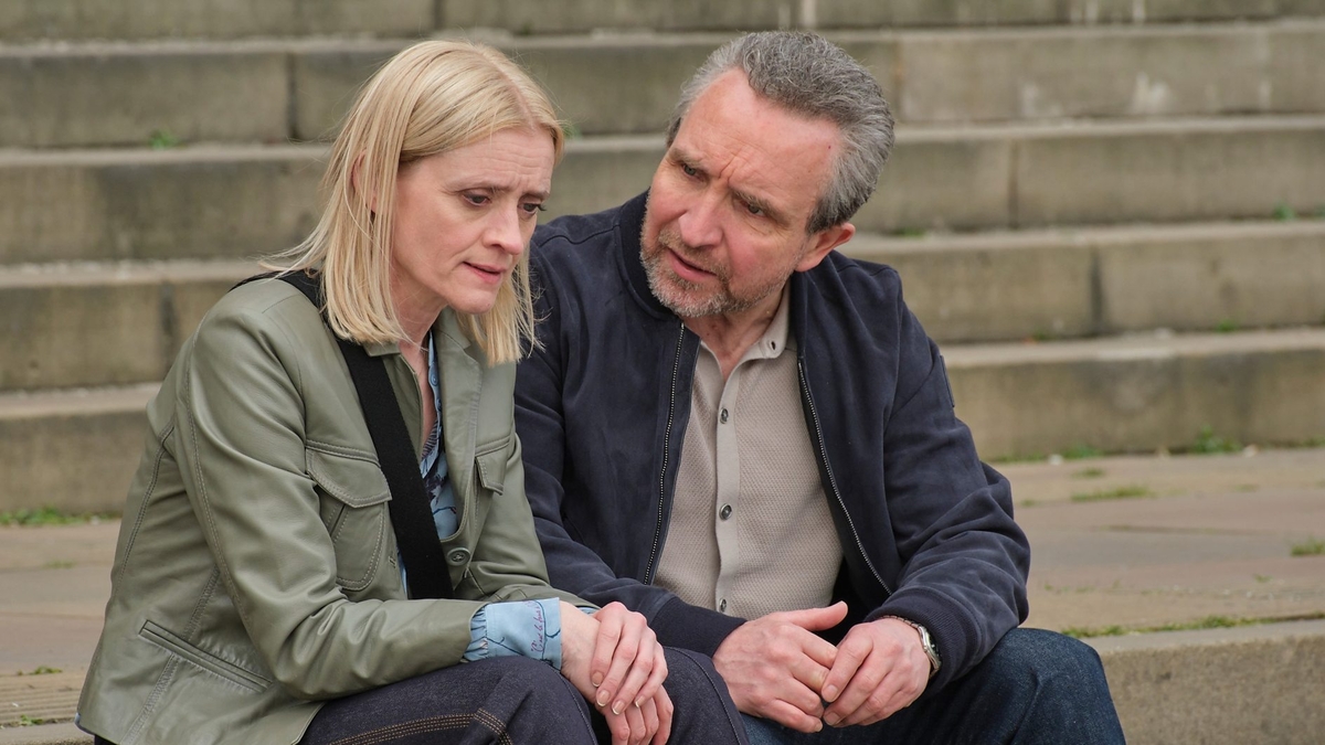 The pair sit outdoors on a cement or stone step, both their brows furrowed in concern. Eddie looks at Anne-Marie, who looks into the middle distance 