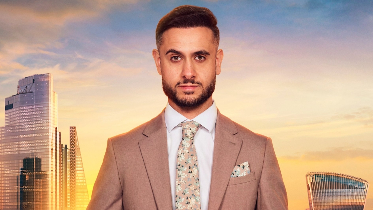 Carlo Brancati looks into the camera in front of the London skyline, wearing a pinkish-brown blazer, white shirt and floral tie and pocket square