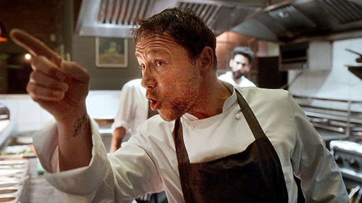 Stephen Graham in chef's whites stands in a professional kitchen with his finger pointed