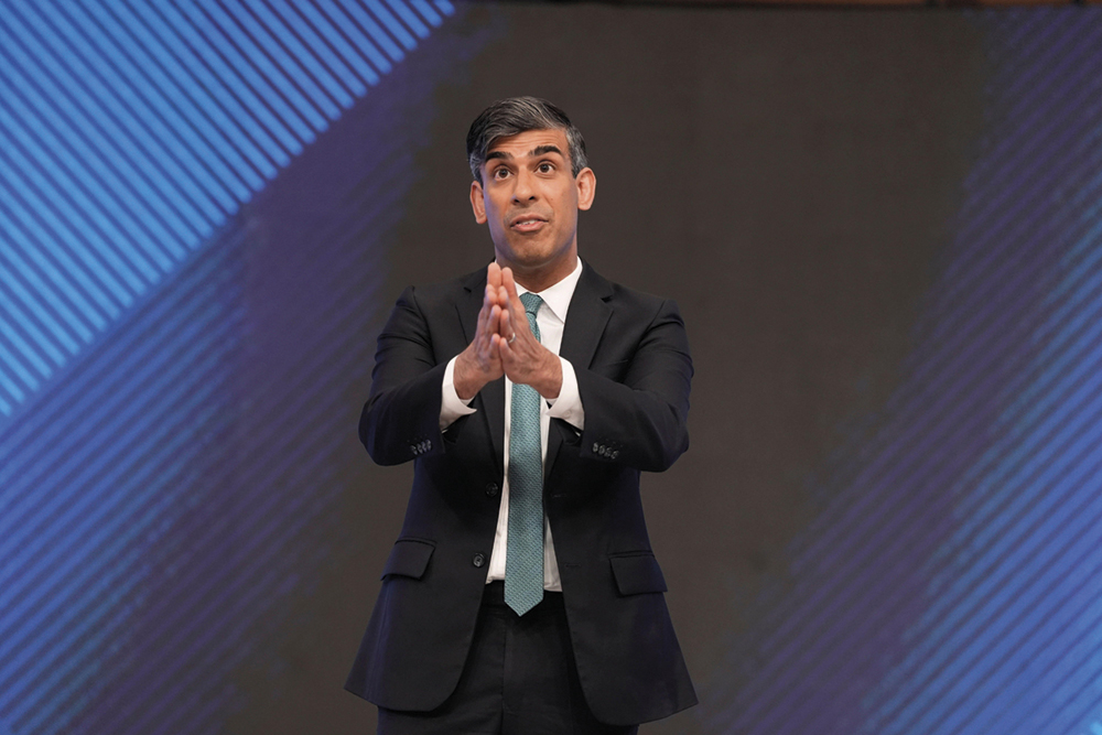 Rishi Sunak delivers a speech, hands clasped together and pointing outward