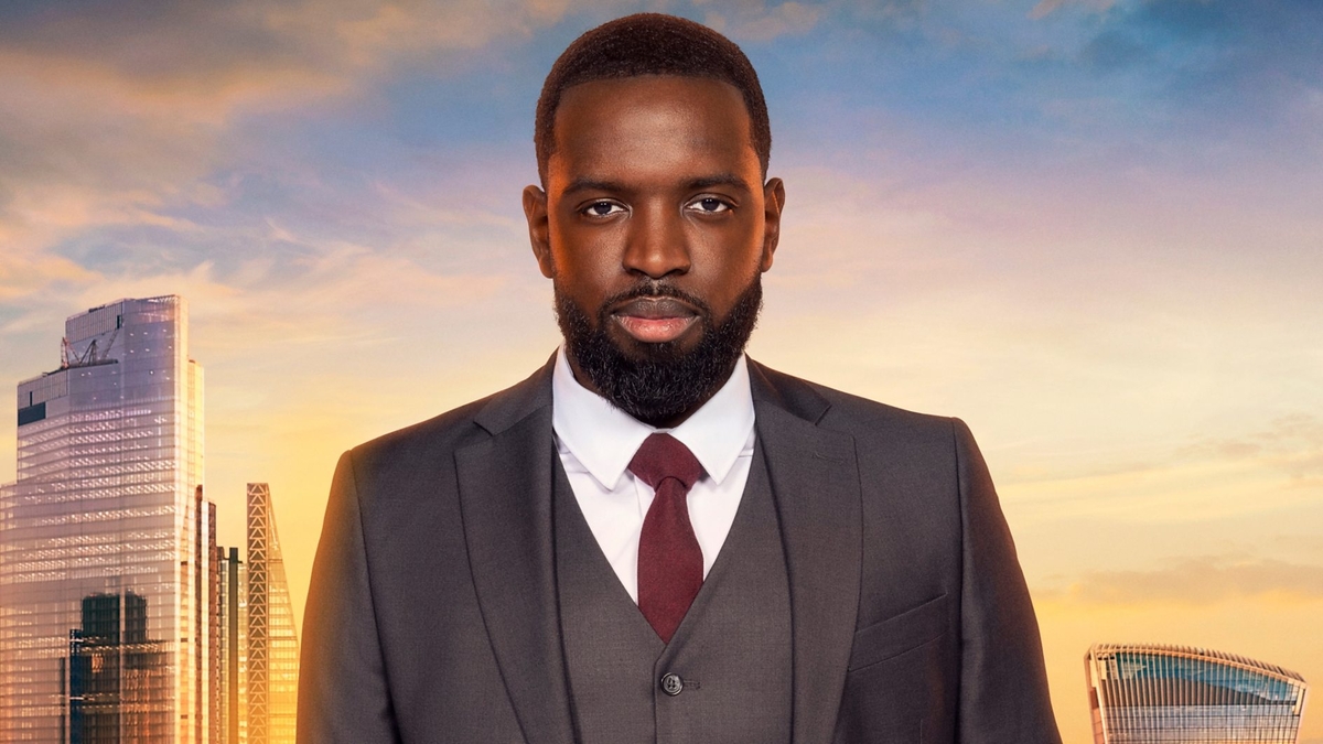 Frederick Afrifa looks into the camera in front of the London skyline, wearing a grey blazer and waistcoat, white shirt and wine-red tie