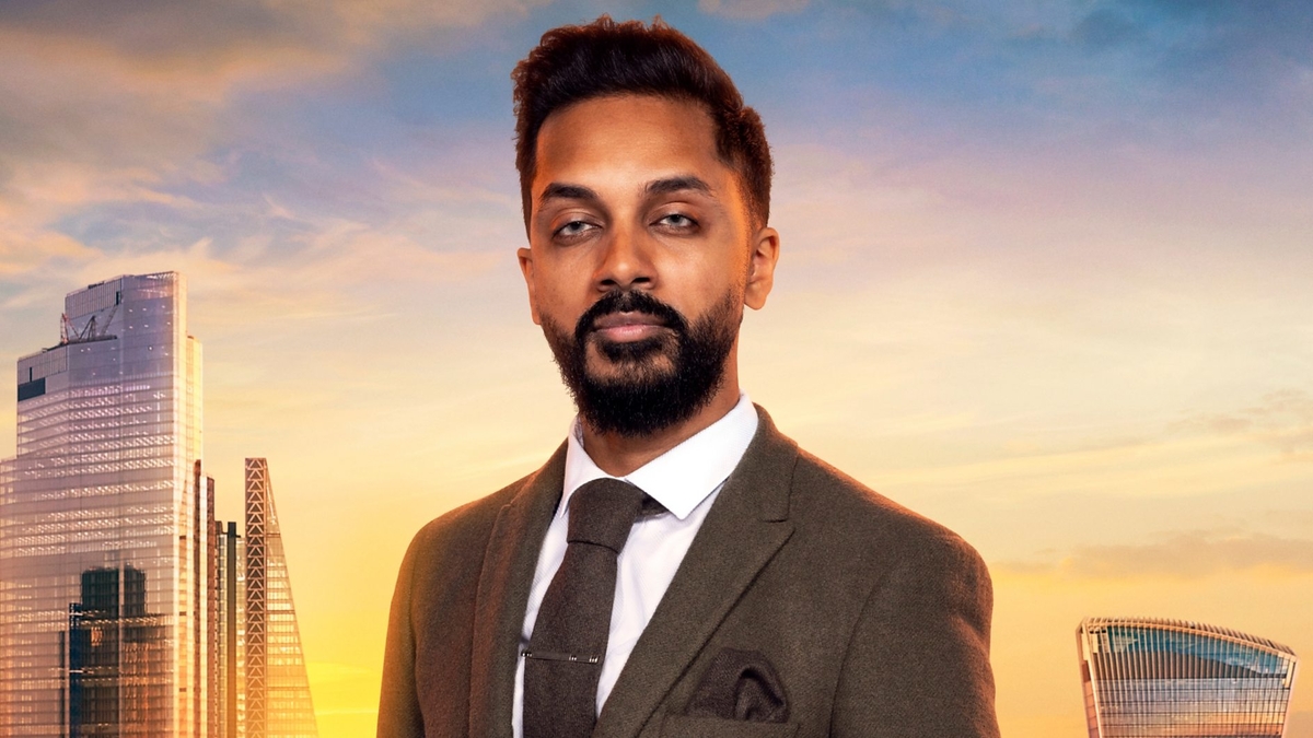 Jana Denzel looks into the camera in front of the London skyline, wearing a textured brown blazer and tie, as well as a brown tie clip and pocket square