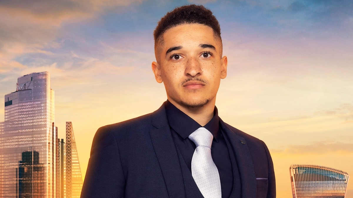 Jordan Dargan looks into the camera in front of the London skyline, wearing a black blazer, waistcoat, shirt and pocket square, as well as a silver tie