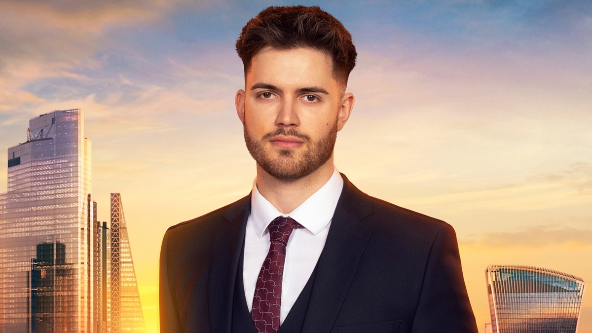 Keir Shave looks into the camera in front of the London skyline, wearing a black blazer and waistcoat, white shirt and red tie with a thin grey recurring pattern over it