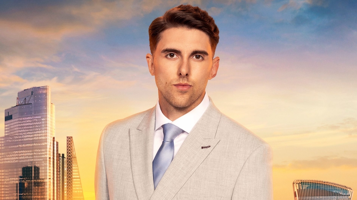 Liam Snellin looks into the camera in front of the London skyline, wearing a grey blazer, white shirt and blue tie