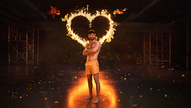 Ciaran Davies stands in front of a heart that has been set on fire, against a black backdrop