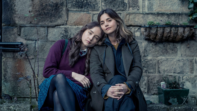 Ruby Stokes as Hannah and Jenna Coleman as Ember sit outdoors, Hannah's head on Ember's shoulder, the two of them looking into the camera