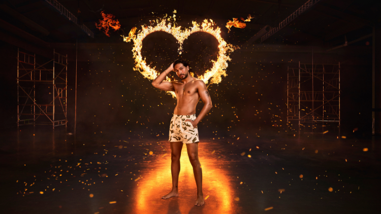 Munveer Jabbal stands in front of a heart that has been set on fire, against a black backdrop