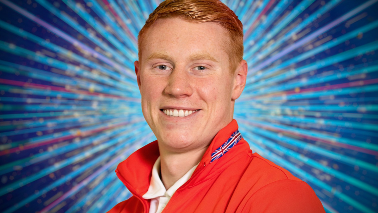 Tom Dean looks into the camera in front of a glittery blue backdrop