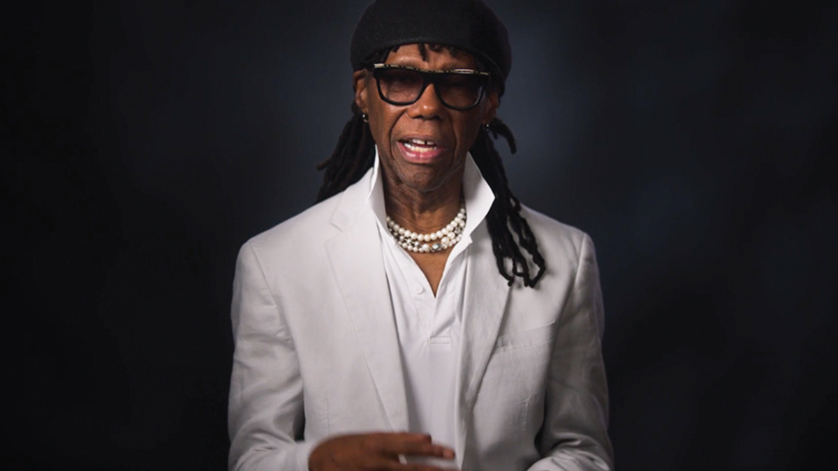 Nile Rodgers sits talking in front of a black backdrop