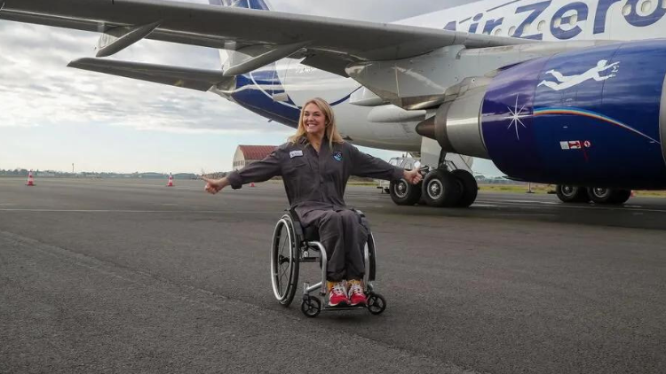 Sophie Morgan sits in a wheelchair in front of a plane, giving two thumbs up