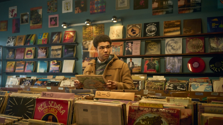 Levi Brown (a black man in his twenties) stands in the middle of a record store, looking over to his left 