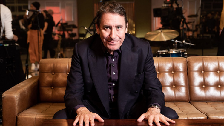 Jools Holland sits on a sofa, splayed hands on a coffee table in front of him