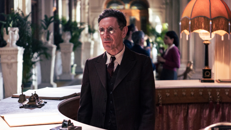 Paul McGann stands inside a circular hotel desk