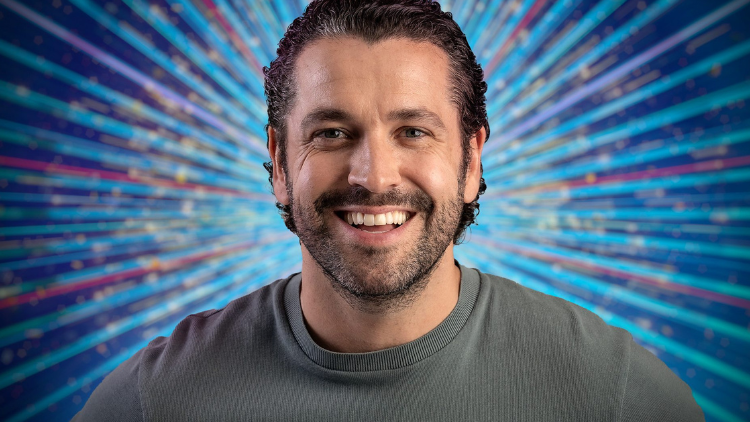 Shane Ward smiles in front of a glittery blue backdrop