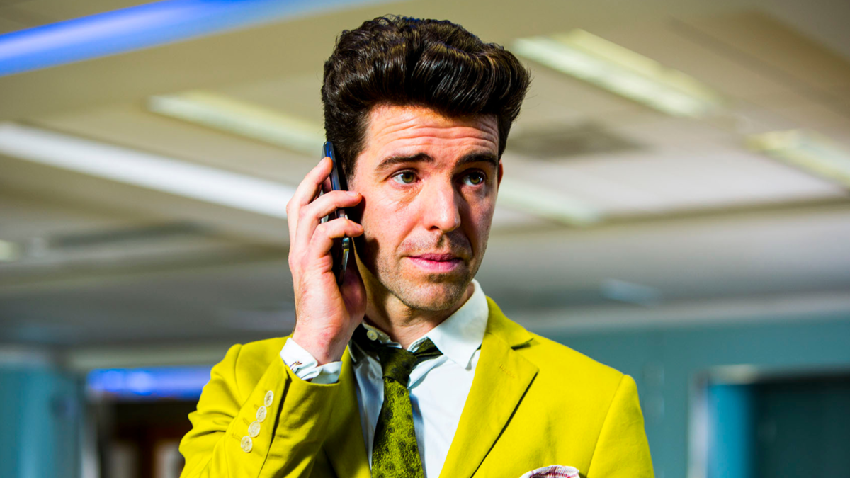 Paul Ready as Lee, on the phone wearing a yellow suit