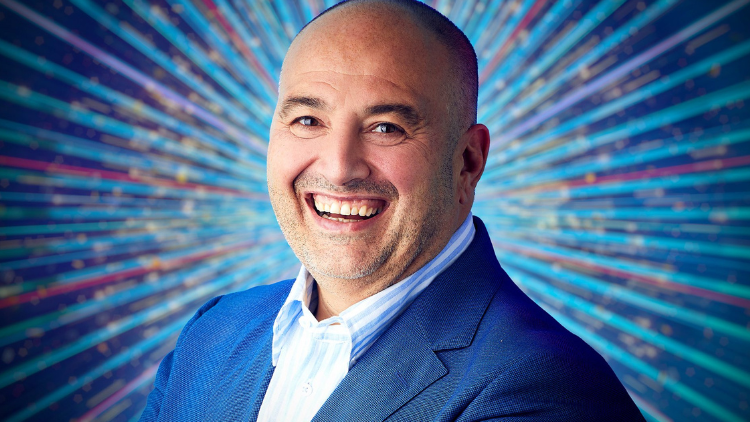 A photo of Wynne Evans in front of a glittery blue backdrop