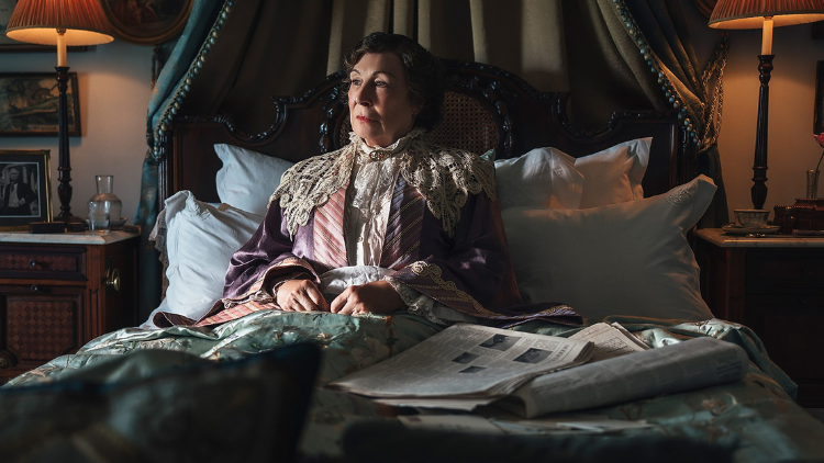 Anjelica Huston lies in bed, with newspapers next to her