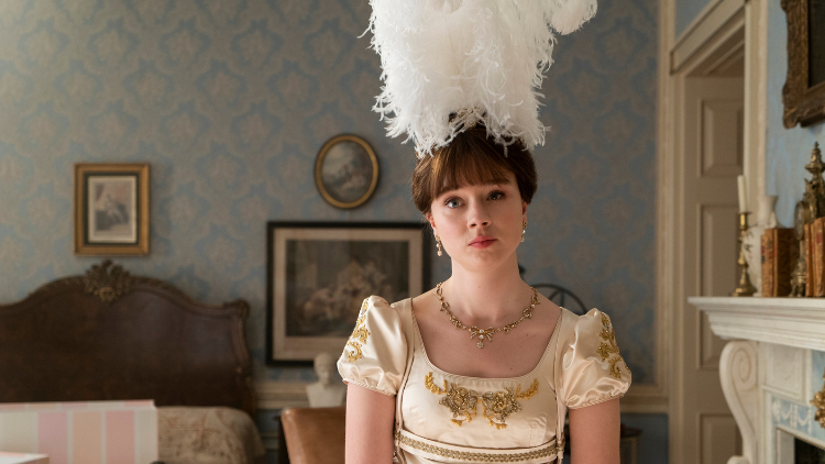 Claudia Jessie as Eloise Bridgerton stands alone in a room, unsmiling and with her head at a slight titlt
