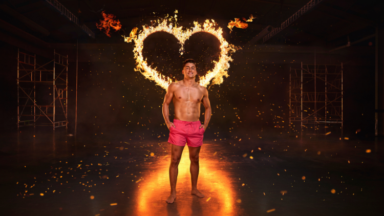 Sean Stone stands in front of a heart that has been set on fire, against a black backdrop