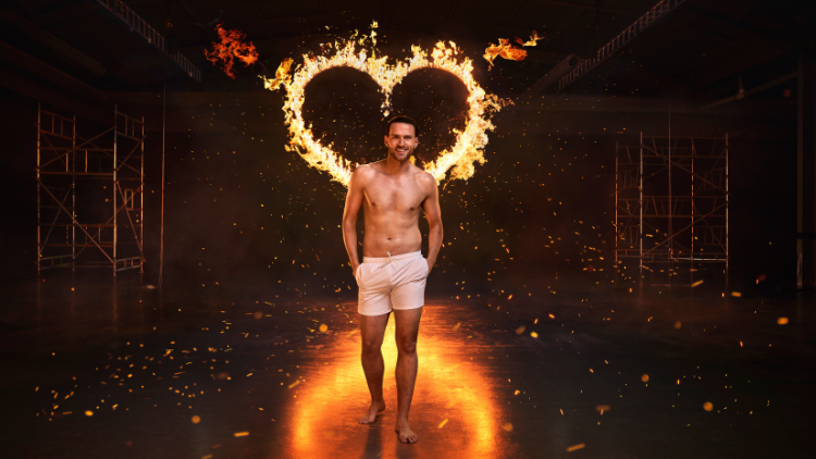 Ronnie Vint stands in front of a heart that has been set on fire, against a black backdrop