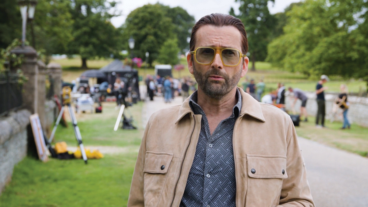 David Tennant stands outdoors, in front of a film crew