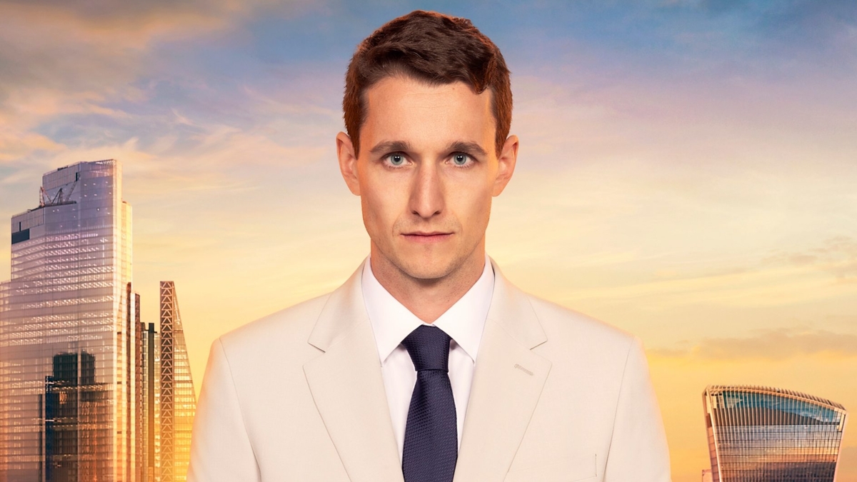 Max England looks into the camera in front of the London skyline, wearing a white shirt, off-white blazer and black tie