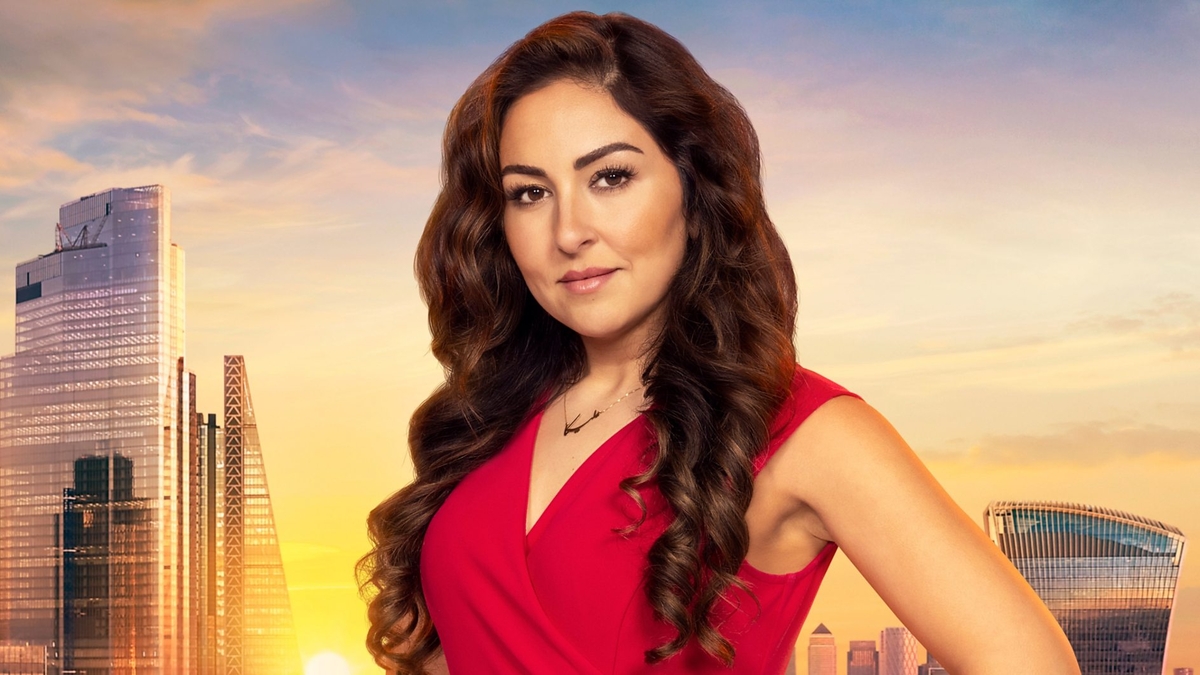 Melica Moshiri looks into the camera in front of the London skyline, wearing a red business-attire dress