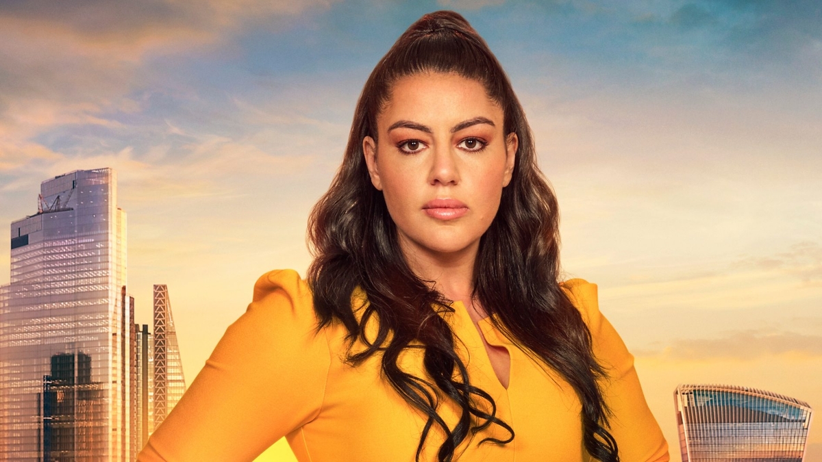 Nadia Suliaman looks into the camera in front of the London skyline, wearing a yellow business-attire dress