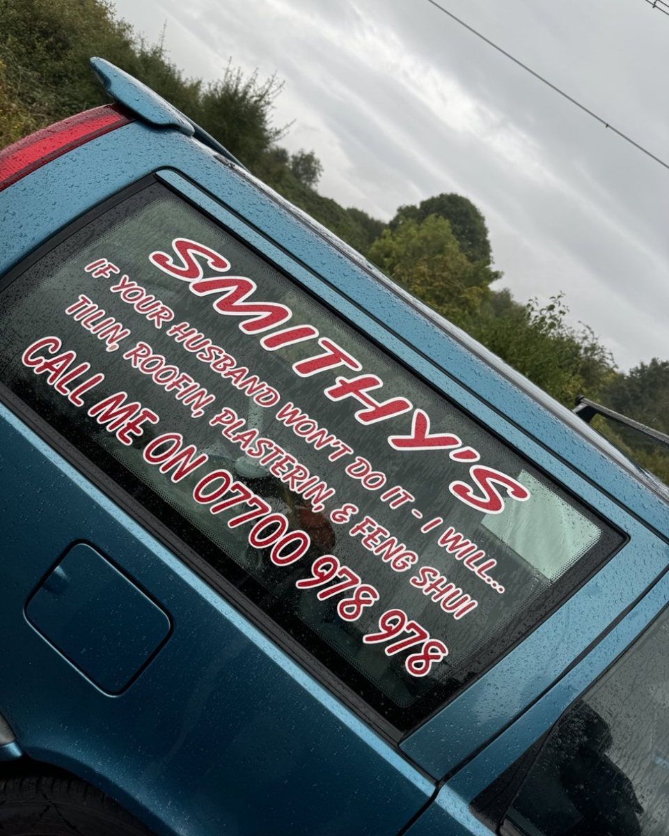 The side of Smithy's car, which has stick-on decal text on the window advertising his business 