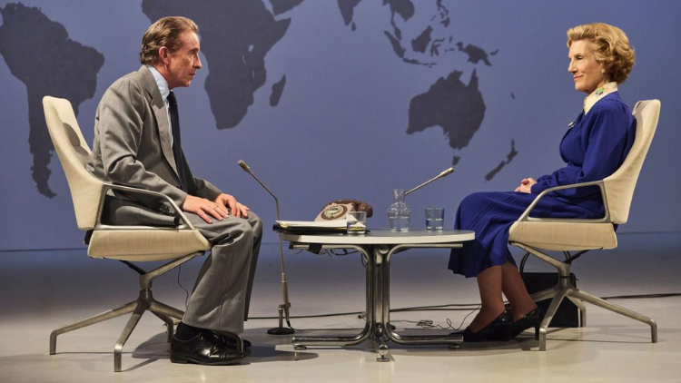 Steve Coogan, a white man in his fifties, sits across from Harriet Walter, a white woman in her seventies in a TV studio. Both wear 1980s businesswear.