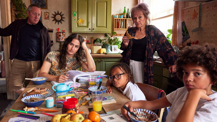 Two children and Macy-Jacob Seelochan sit at a dining table, a man and a woman standing above them 