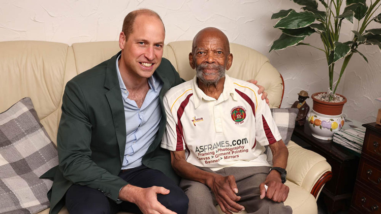 Prince William sits with his arm around a member of the Windrush Generation