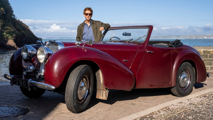 Damien Molony poses behind a 1940s Triumph Roadaster, wearing sunglasses