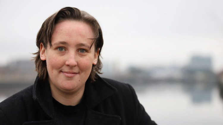 Black, a white woman in her twenties, looks into the camera and smiles, stood outdoors