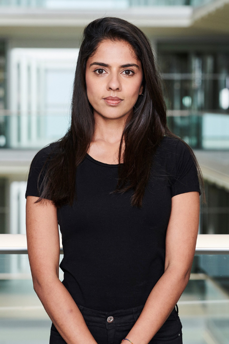 Ria Chatterjee looks into the camera, in front of a blurred office background