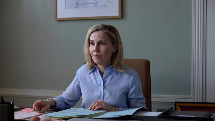 A character played by Sally Phillips sits behind a desk, looking mildly concerned