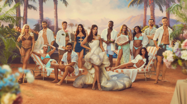 Host Maya Jama (medium skin tone with brown long hair) stands in front of the cast, who are all various skin tones, heights, and all wear swimwear. They stand in a tropical scene.