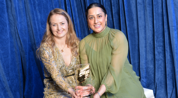 Two women pose with their RTS Craft & Design award: on the left, a woman with long blonde curly hair wearing a sparkly dress smiles, and on the right, a woman with dark brown hair in a green dress smiles