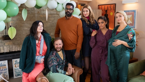 Aisling Bea, Colin Hoult, Romesh Ranganathan, Jessica Knappett, Mandeep Dhillon and Lisa McGrillis sit and stand around a chair in a living room, which is decked out with balloons