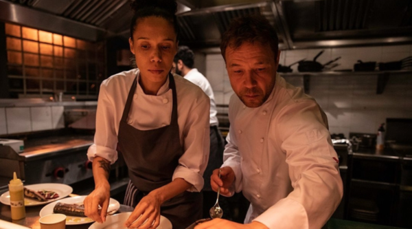 A female and male chef in chef whites prepare plates in a restaurant 