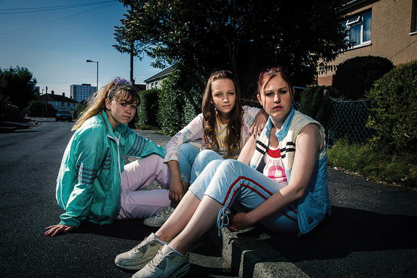 The cast of Three Girls sit on a curb