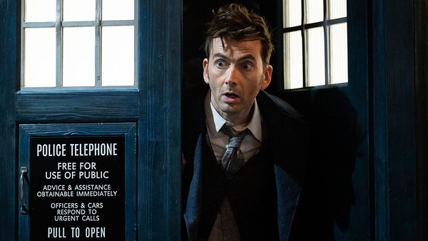 The Doctor, played by David Tennant, leans out of the TARDIS with a look of shock on his face