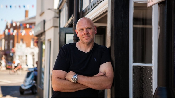 Tom Kerridge is in a black top and stands outside a shop