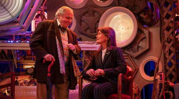 In the TARDIS, the Seventh Doctor, played by Sylvester McCoy, stands next to Ace, played by Sophie Aldred, who is sat down
