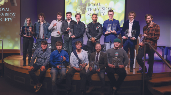 A group of students hold up RTS Awards in front of screens displaying the RTS branding