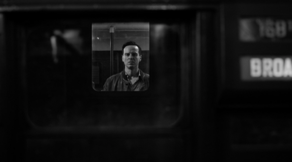 Andrew Scott, in character as Tom Ripley, looks out from a train window, looking menacing, in black and white