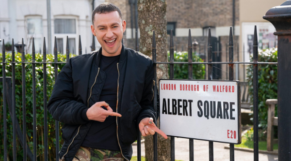 Olly Alexander points excitedly at the street sign for Albert Square